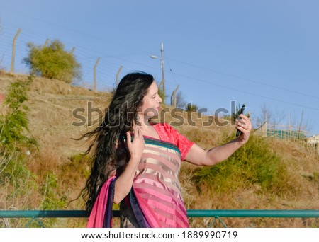 A lady wearing indian dress holding a mobile phone in her hand.