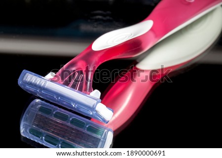 Colored plastic razor on black background with reflection