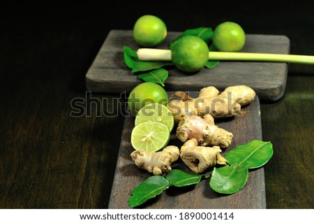 Lime, ginger, lemongrass and lime leaves on a wooden cutting board on a black background