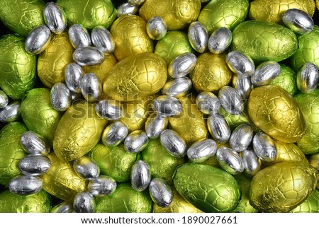 Large and small yellow, gold, green, lime green and silver spring colours of foil wrapped chocolate easter eggs, against a black background.