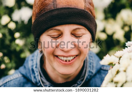Beautiful European woman in the garden near the flowers. White, pink bushes of aster flowers. Senior middle-aged woman without makeup. Emotional, sincere smile, rejoices in life. Eco, care