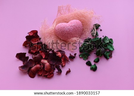 Pink heart on soft hay. Red and green dry flower petals. Holiday concept - Valentine's Day.
