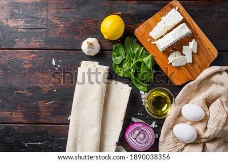 Greek spanakopita ingredients filo spinach eggs feta top view on dark wooden background space for text Royalty-Free Stock Photo #1890038356