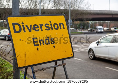 A road sign that reads diversion ends at a roundabout with cars moving in the background