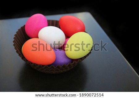 Multi colored painted easter eggs in red, pink, yellow, green and white in a brown paper basket against a dark background. 