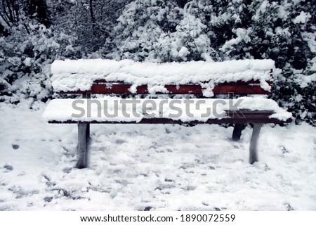 Snow-covered bench during cold German winter. Landscape and nature with snow and ice. Rest area inside city park.