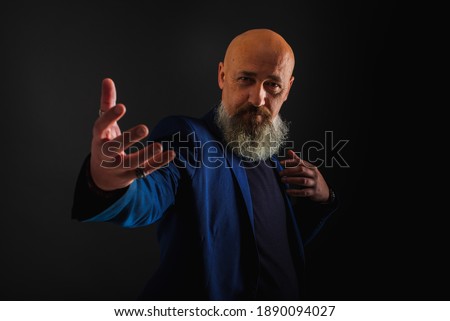 Smiling business man with beard showing man, gesturing with hands, showing something, isolated on dark background. Low key. The portrait is emotional