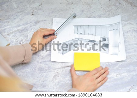 On the table is a mock-up of a kitchen, an example of a palette of facades and drawer bodies and a handle for the door. girl orders furniture for the kitchen in the salon. Home improvement concept