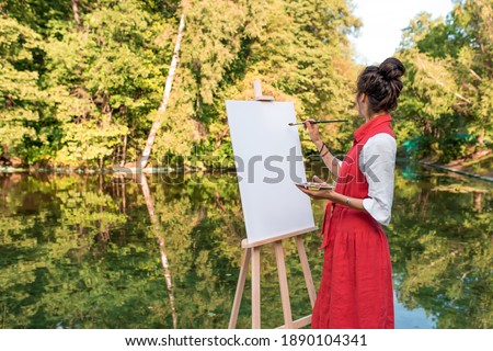 free space for text, woman artist summer park near lake, river pond, draws picture, white canvas. Creation creativity, art fantasy. Mirror reflection in water, brush colored paints girl.