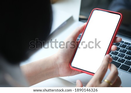 Close up view of young woman hands holding mock up smart phone with blank white screen at her workspace.