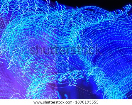 Wavy light trails in an ornamental garden with festive holiday illumination at night. Long exposure with motion blur. Light painting.