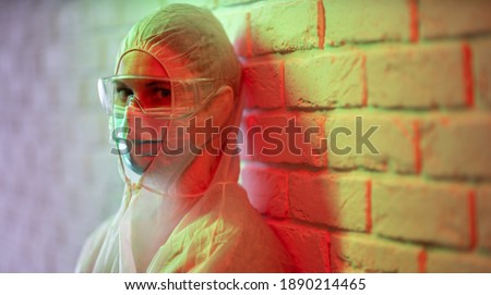 Doctor in protective suit on background of brick wall in red zone.
