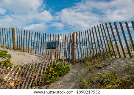 Artistic background of a wind fence protecting Florida sand dunes  with a warning sign and vegetation on cloudy blue sky.