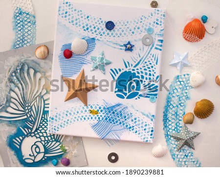 canvas with stencil printed fish drawing. Clam shells glazed with acrylic paint. Summer theme craft.