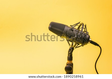Modern condenser microphone on a stand on a yellow background. Sound recording equipment.