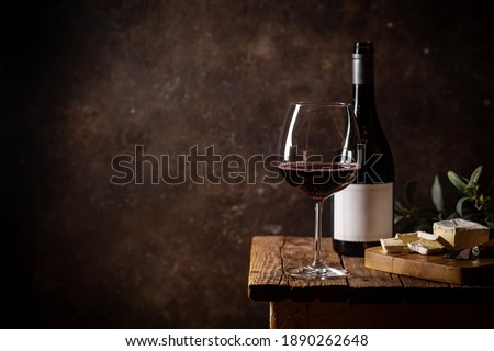 Glass of red wine with bottle and cheese against rustic dark wooden background