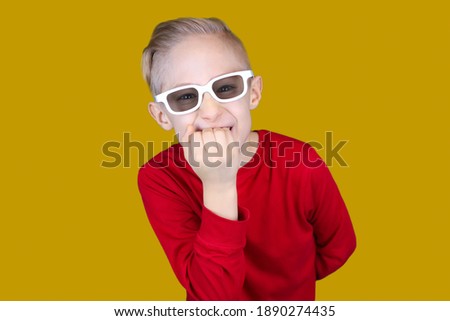 a child in children's 3D glasses bites his nails in surprise