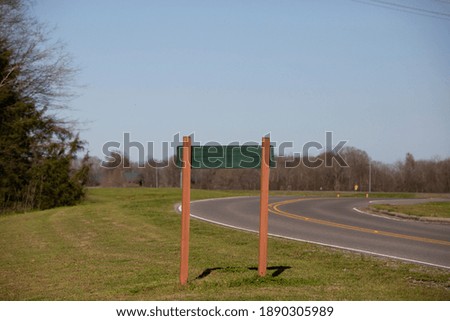 Back of a green and tan sign in the grass near a winding highway