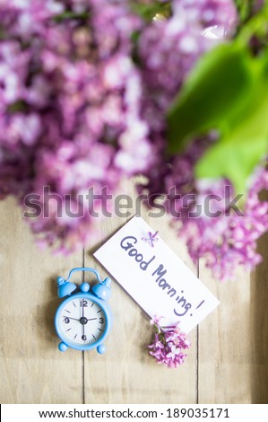 Good morning note, lilac flowers and old-styled clock on the wooden table