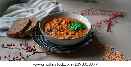 Close up picture of amazing vegetable lentil soup with carrot, onion, potatoes and chickpeas decorated on natural brown table background. Autumn winter season healthy homemade soup with fresh basil.