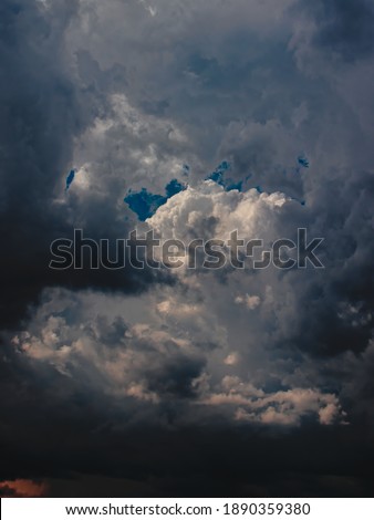 portrait image of white cumulus cloud illuminated by the sun, surrounded by swirling gray clouds.