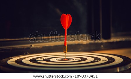 Dart arrow hit on bulleyes of dartboard to represent that the business reached the target  with dark tone picture style. Target and goal as concept.