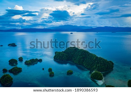 Drone picture on sunset time of islets in soccoro island, philippines, with some trees, a tiny beach on the bottom right side of the picture, some mountains and clouds in the background 