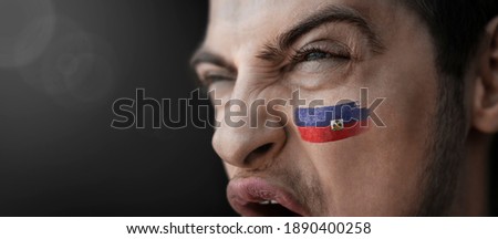 A screaming man with the image of the Haiti national flag on his face.
