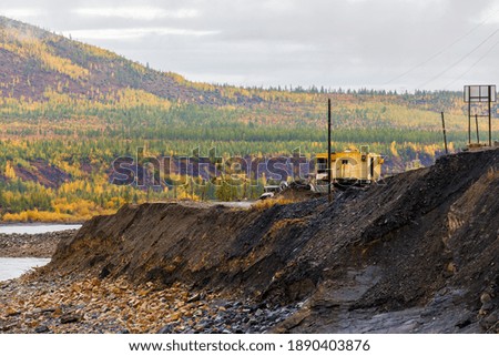 Magadan, Russia - Construction of the Ust-Srednekanskaya hydroelectric station. A bulldozer stands on the edge of a cliff, dug a quarry against the backdrop of autumn hills and smooth water