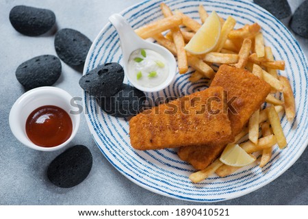 Fish and chips with dips served on a blue and white plate, studio shot on a light-blue stone surface