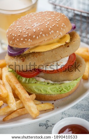 Closeup of double burger with sesame bun, fish cutlets, vegetables and french fries, vertical shot, selective focus