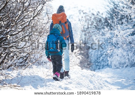 Woman with a child on a winter hike in the mountains, The boy travels with mother in the cold season, A child with a backpack walks with mother in a snowy park, Trekking with children, Winter trip.