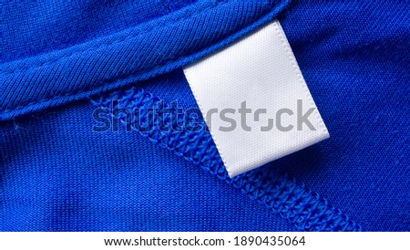 Blank white laundry care clothes label on blue fabric texture background