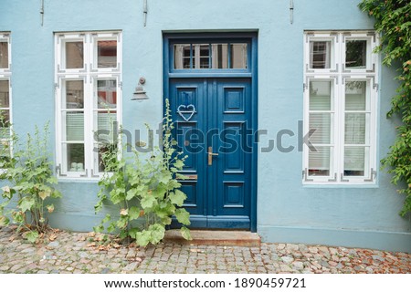 Blue house wall with a blue wooden door and a green plant at the entrance. House in Germany Royalty-Free Stock Photo #1890459721