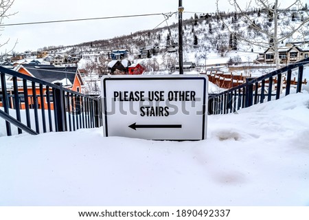 Please Use Other Stairs sign on an impassable stairway in the snowy neighborhood