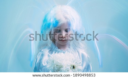 Angel girl. Child art portrait. Heaven blessing. Ethereal aura. Sweet blonde little kid with white flowers in blur iridescent fluorescent glow strokes on blue copy space background.