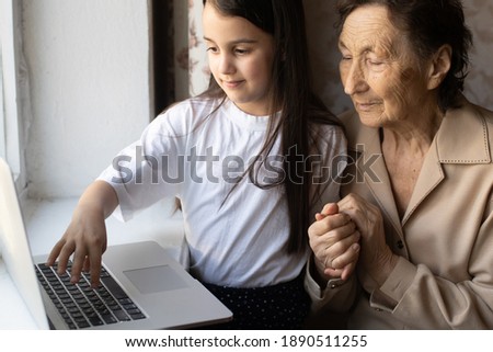 Happy senior woman sitting with her granddaughter looking at laptop making video call. Mature lady talking to webcam, doing online chat at home during self isolation. Family time during Corona