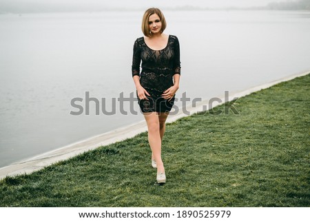 Portrait of a young beautiful European woman with makeup in a black dress standing on the urban street in the city near lake. European girl, beauty, fashion, dark makeup. Bob haircut