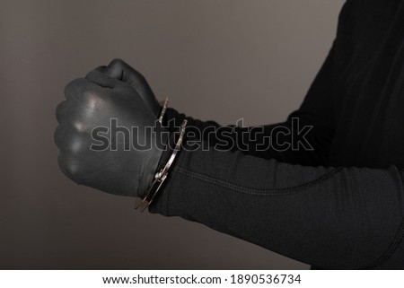 Close up picture of robbers hands with black gloves wearing handcuffs