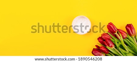 Banner with a bouquet of flowers and a jar of body or face care cream on a yellow background with copy space, text place. Holiday business card. Cosmetics store. Spa treatments. Massage cream. Mockup.