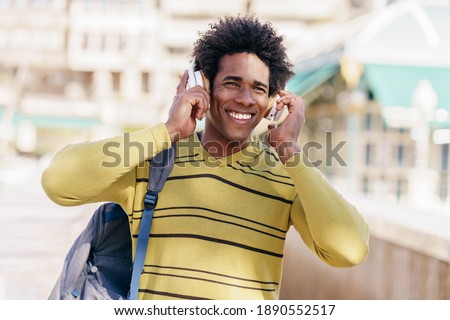 Young Black man with afro hairstyle listening to music with wireless headphones sightseeing in Granada, Andalusia, Spain.
