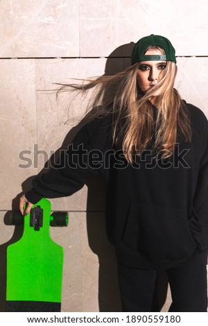 Young woman dressed in black with a green longboard at the street