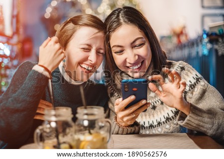 Two funny female friends look at new memes on social networks and laugh out loud in cafe. Smartphone with online Internet access - a new type of leisure for group of friends Royalty-Free Stock Photo #1890562576