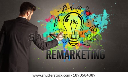 businessman drawing colorful light bulb with REMARKETING inscription on textured concrete wall, new business idea concept