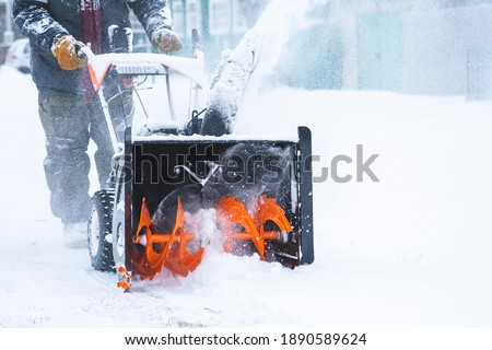 a man removes snow with a snow plow after a heavy snowfall near his house, close-up, blizzard, snow in the lens, selective focus, snow Royalty-Free Stock Photo #1890589624