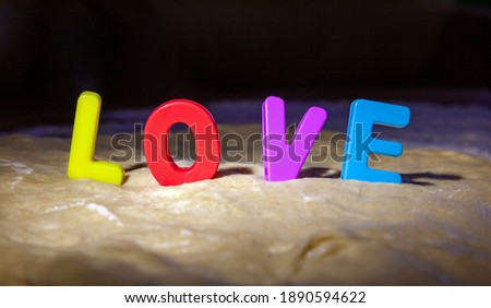 Colorful plastic letters stand among the fresh dough and make up the word Love. Making pies and other baked goods at home. Hard light