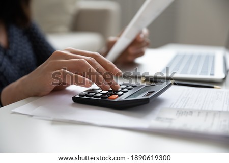 Close up young mixed race woman calculating domestic expenses involved in financial paperwork indoors, focused lady managing monthly banking payments summarizing utility bills and taxes at home. Royalty-Free Stock Photo #1890619300
