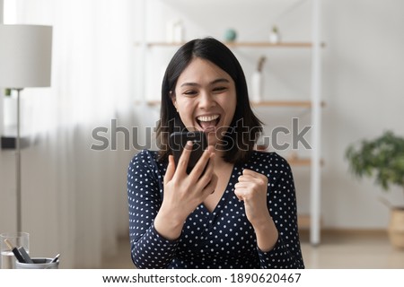Emotional happy millennial korean ethnicity woman looking at smartphone screen, reading message with unbelievable amazing news, celebrating getting online shopping prize or lottery win notification. Royalty-Free Stock Photo #1890620467