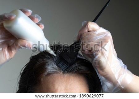 Closeup woman hands dyeing hair using black brush. Middle age woman colouring dark hair with gray roots at home Royalty-Free Stock Photo #1890629077
