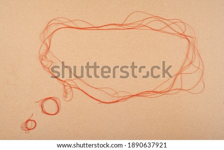 Speech or think bubble made of thread, red rope. Thematical copy space on cardboard textured background